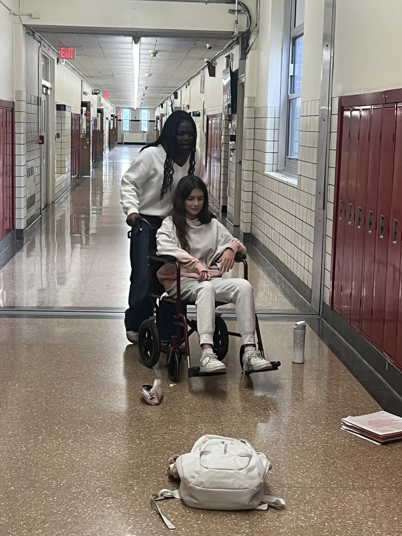 Two students in a school hallway, one seated in a wheelchair